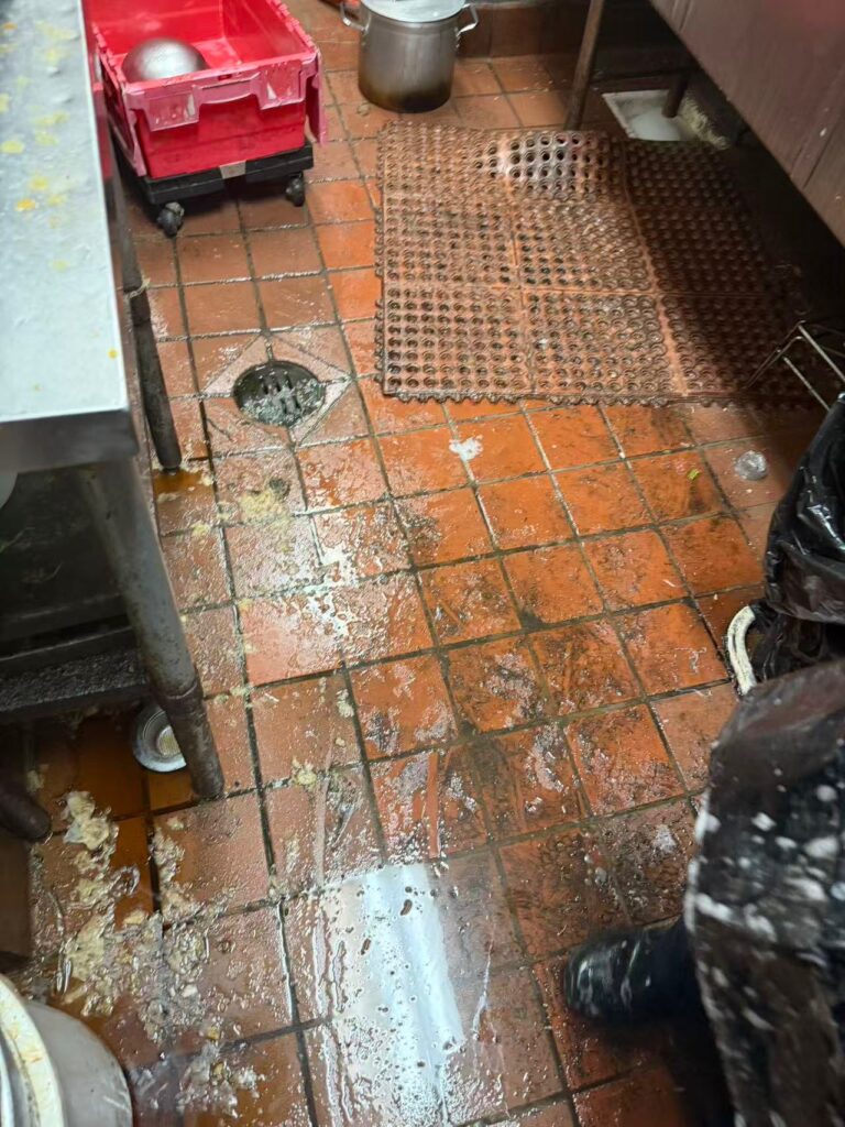 Messy grease spill on a commercial kitchen floor requiring proper grease spill clean up to reduce slip hazards.