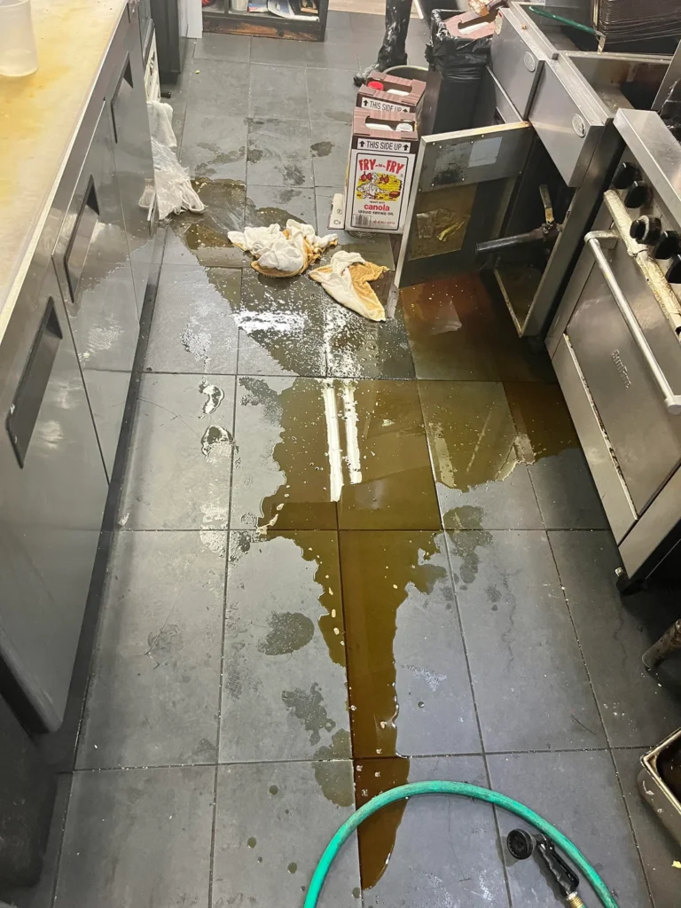 Used fryer oil spilled on a commercial kitchen floor requiring proper grease spill clean up to reduce slip hazards.