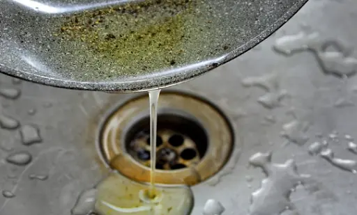 Pouring hot grease into a kitchen sink as improper waste cooking oil disposal